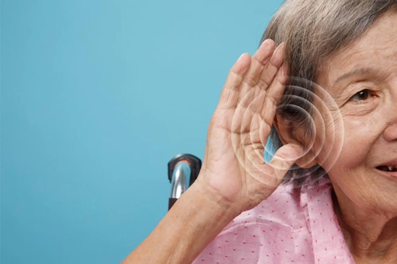 An older woman in a wheelchair holds up a hand to express hearing loss