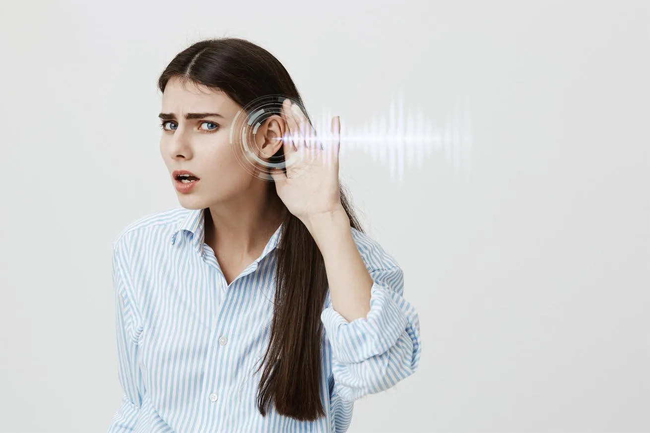 A woman experiencing hearing issues raises her hand to her ear