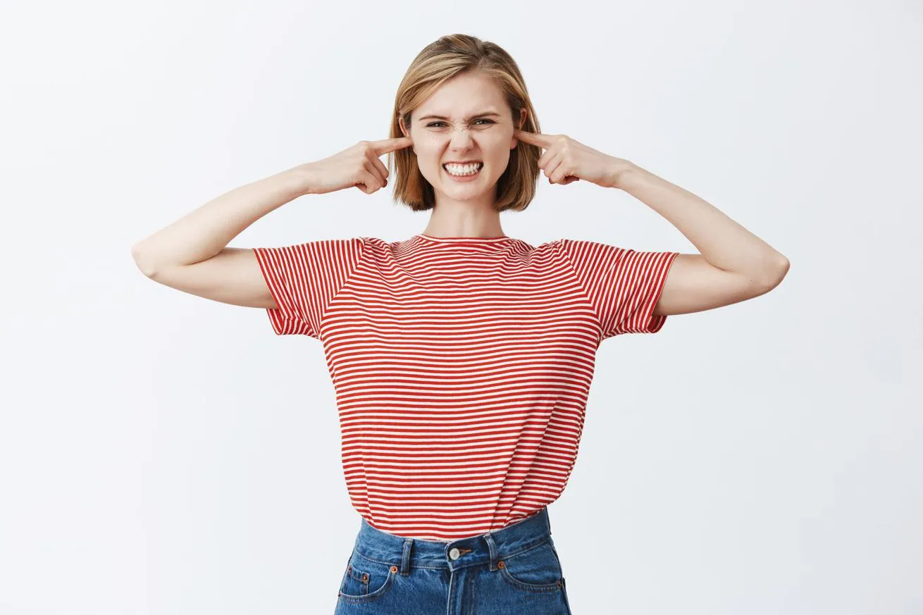 A young woman experiencing tinnitus puts her fingers in her ears