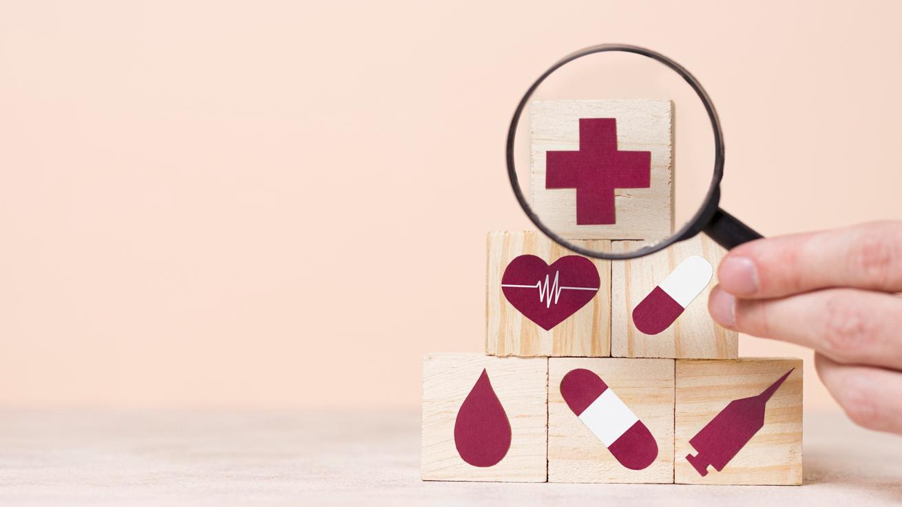 A magnifying glass held up in front of blocks with healthcare symbols