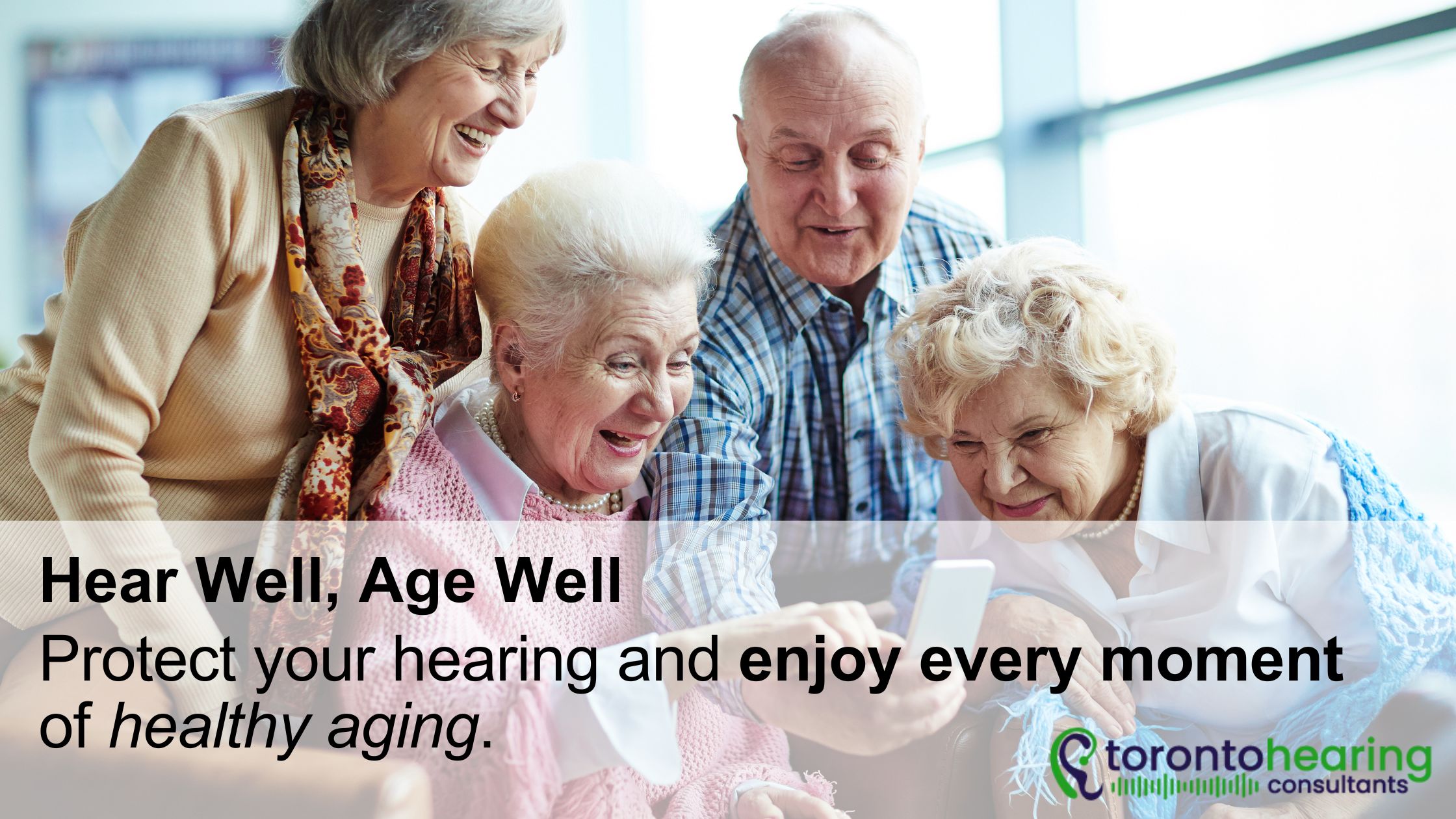 Group of seniors enjoying time together and smiling while looking at a phone, promoting healthy hearing and aging with Toronto Hearing Consultants.