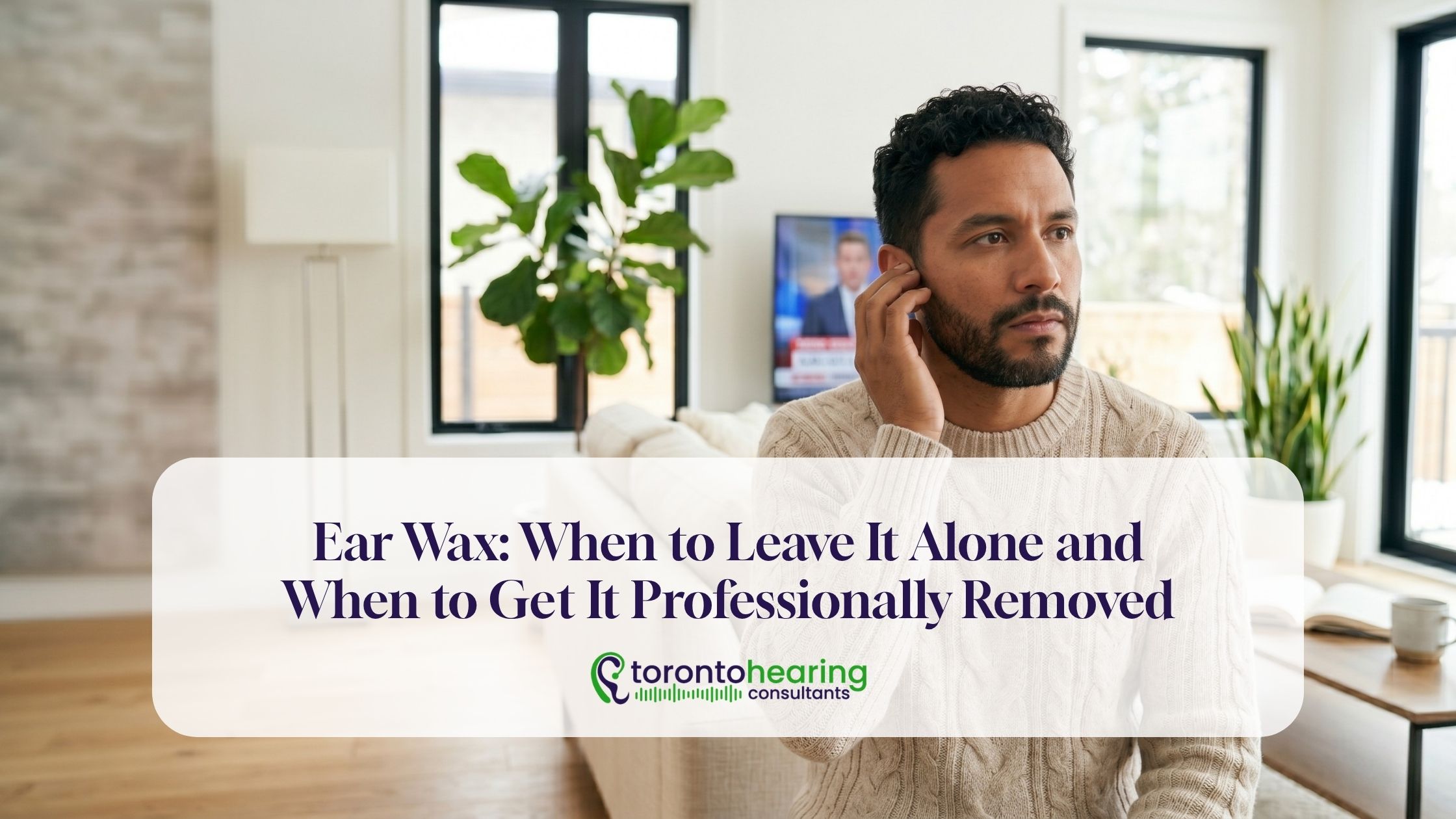 Man touching his ear at home while experiencing symptoms that may indicate ear wax buildup requiring professional assessment or removal